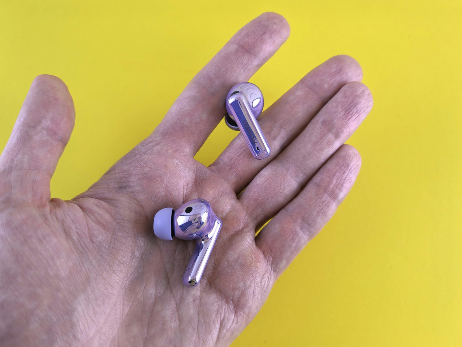 A hand holding a pair of silver ear buds